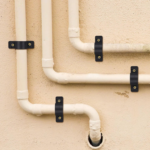 1/2 inch pipe support clamps, black metal with screws, securing white PVC pipes to a wall