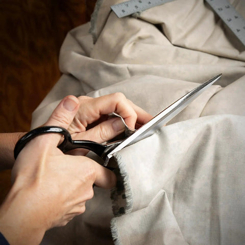 Hands using 10 Inch Bent Handle Industrial Shears for Heavy Duty Cutting of Upholstery, Carpet, and Drapery Materials on fabric.