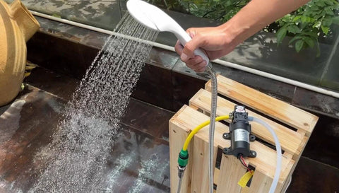 bayite 12V DC Water Transfer Pump with 2 Hose Clamps 12 Volt Diaphragm Pump in use, spraying water outdoors from a handheld nozzle