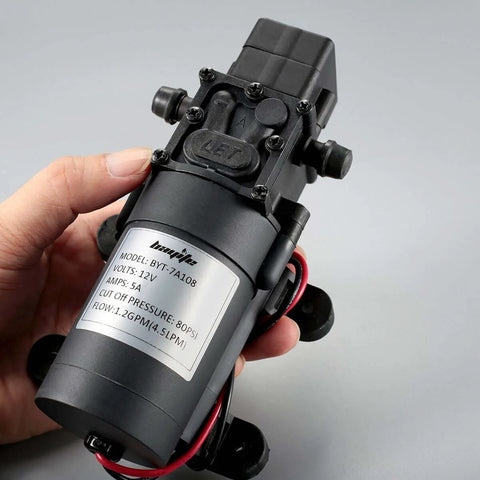 Hand holding bayite 12V DC Water Transfer Pump with 2 Hose Clamps 12 Volt Diaphragm Pump Self Priming Sprayer Pump with Pressure Switch