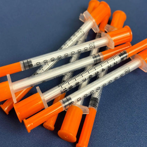 1cc Syringes With 31G Needle 5/16 Inch 8mm Individually Packaged 36 For Lab Use And Calibration, orange capped, scattered on blue surface