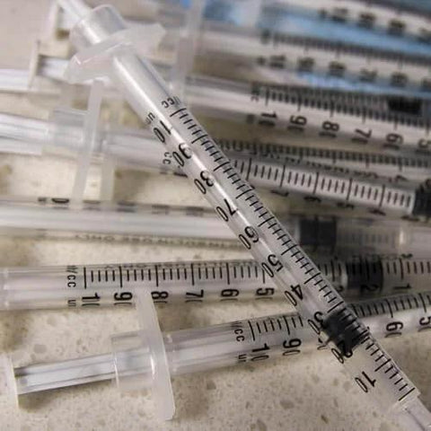Pile of 1 mL Syringes With 31G Needle Five Sixteenth Inch Length Individually Wrapped Pack Of 100 For Lab Use scattered on a surface.