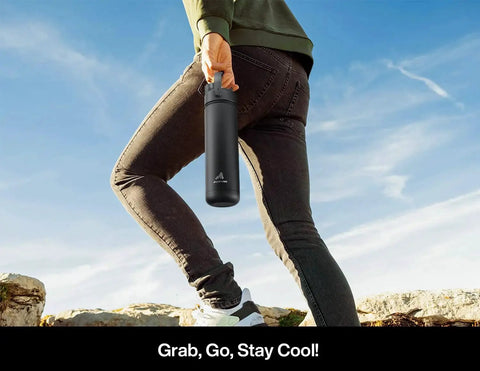 Person holding a black 26 oz insulated stainless steel water bottle with a 2-in-1 straw and spout lid, perfect for outdoor activities.