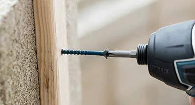 Close-up of 1/4 Inch Hex Washer Head Concrete Screw For Masonry, Brick And Block being installed with a drill into wood and concrete