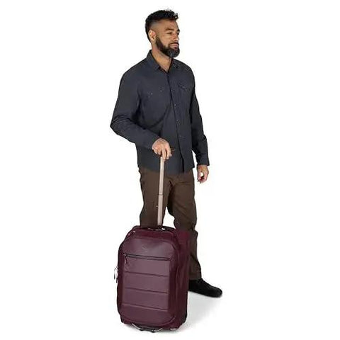 Man holding Ozone 2-Wheel Carry-On Luggage with oversized wheels and telescoping handle from Osprey, in airline-approved cabin size.