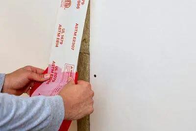 Applying Fire and Water Barrier Tape FWBT4 4 in x 75 ft to a construction joint for smoke and sound isolation.