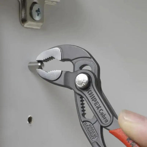 Cobra Water Pump Pliers, 5 Inch, Red, Adjustable Pliers With Self-Locking Teeth in use on pipe with pinch guard feature visible
