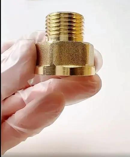 Brass pipe reducer adapter close-up held by gloved hand, threaded male connector and hex body