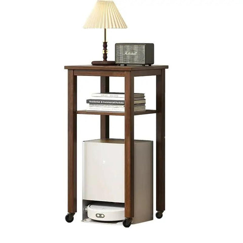 Wooden side table on caster wheels with a lamp, radio, books, and storage space for a vacuum beneath.