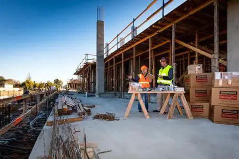 Construction site with workers discussing plans near materials and partially built structure.