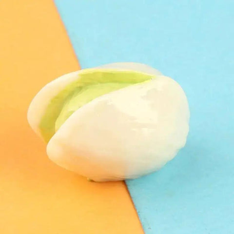 Close-up of a single resin pistachio from the 15-Piece Realistic Miniature Nut Set For Dollhouses on a colorful background.
