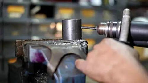 Close-up of hand using 1/8 In NPT Pipe Tap And R HSS Drill Bit Set In Carbon Steel, Black Oxide Finish on metal pipe in vice
