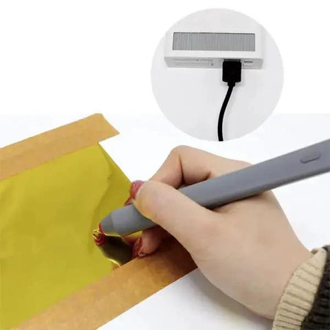 Foil Quill Pen Starter Kit With Four Metal Tips, USB Powered, Gray Finish, Includes Heat Activated Foil Roll 3m By 0.15m For Card Making And Scrapbooking in use on gold foil, USB connection shown. Hand holding gray pen tool.
