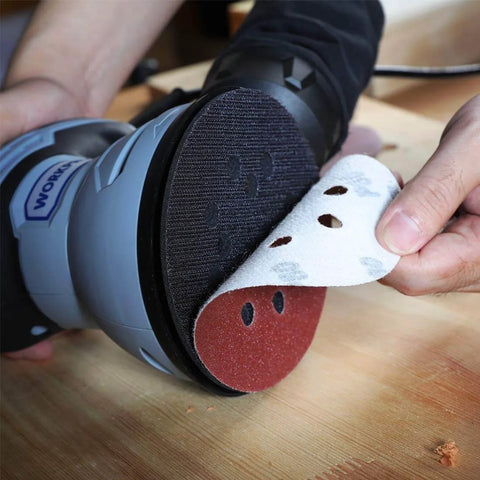 Applying 150 Piece Sanding Discs Set 5 Inch 8 Hole Grits 60 To 600 to a random orbital sander on a wooden surface