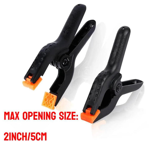 Two black 4.5 inch plastic spring clamps with orange tips, highlighting Ten Pack Heavy Duty 4.5 Inch Plastic Spring Clamps For Crafts Backdrops Photography And Home Improvement Projects Durable Nylon Construction With Ergonomic Round Handles And Anti Slip Grip.