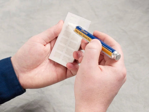 Fluke Networks NFC-SOLVENTPEN fiber optic cleaning solvent pen (blue/yellow) beside a white card holder.