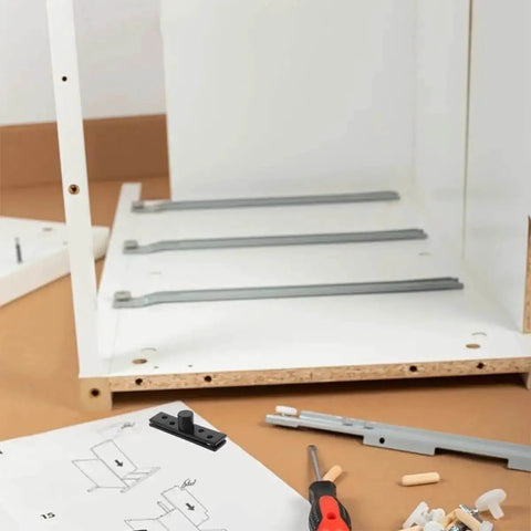 Furniture assembly scene with tools and instructions, showing partial cabinet construction with components spread out on the floor.