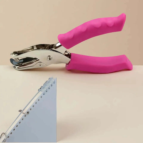 1/4 Inch Pink Handheld Circle Hole Punch For Crafting placed on table next to punched cardstock, showing grip and metal head.