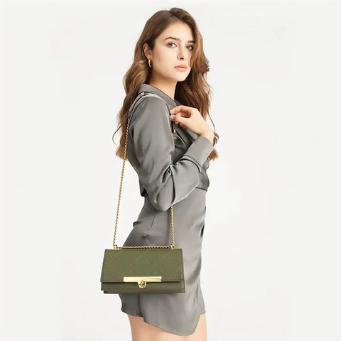 Woman in gray dress holding a green handbag with a gold chain and clasp.