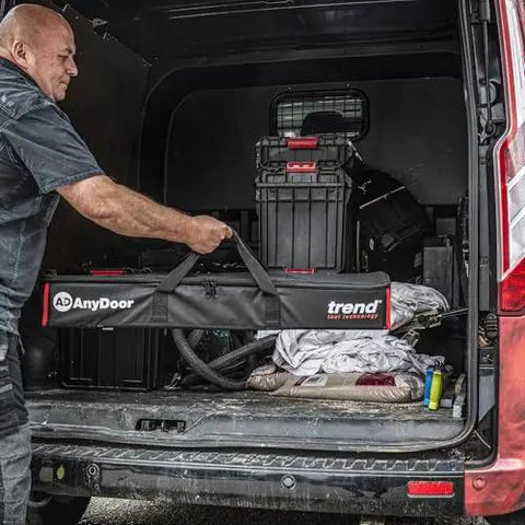 Man loading All-In-One Adjustable Door Hinge Jig Installation Kit For 2 Ft 6 In To 9 Ft Doors into a van, showing the carry case.