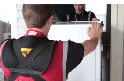 Shoulder Dolly 3500 heavy-duty lifting system in use by two people to lift a white appliance; black padded straps visible