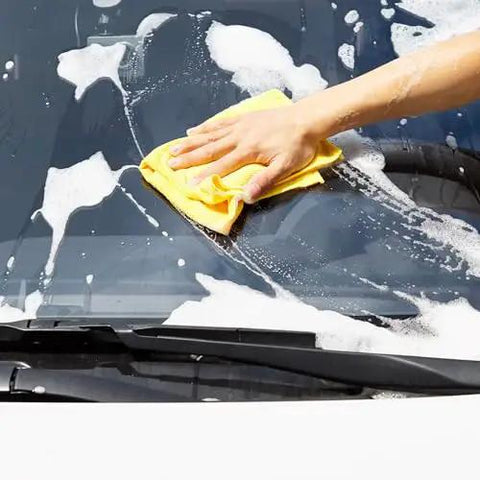 Person using a yellow Ultra Absorbent Microfiber Cleaning Cloths For Cars And Home Go To to wash a car windshield.