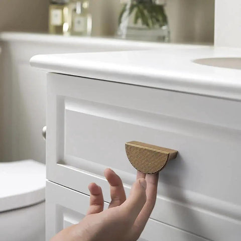 Hand reaching for antique brass zinc alloy cabinet pull 2.5 inch hole center 64mm striped decorative handle installed on white drawer.