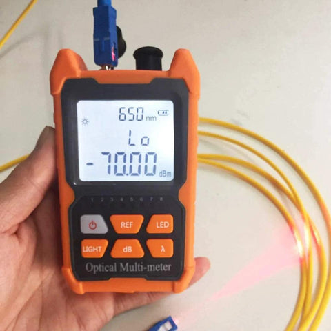 Orange handheld optical multi-meter with LCD readout showing 650 nm, connected yellow fiber optic cable.