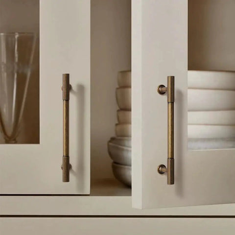 Close-up of 6 pack antique brass kitchen cabinet pulls with 5 inch center to center spacing on cream cupboard doors
