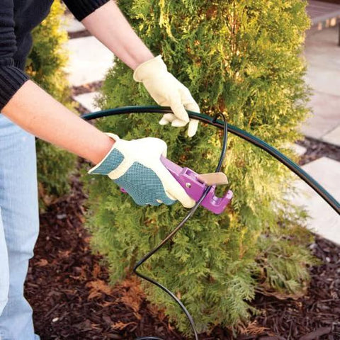Rain Bird 1/4 in drip irrigation tubing, black, 250 ft roll, being installed with a purple fitting by gloved hands outdoors.