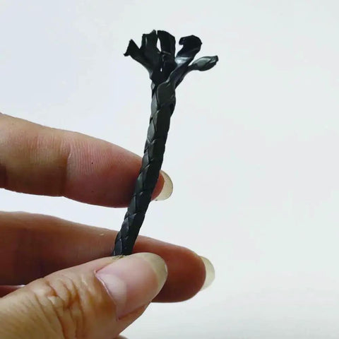 Person holding a piece of Graphitized Expanded PTFE Graphite Braided Compression Packing One Eighth Inch By One Eighth Inch Ten Feet Long For Pumps Valves Mechanical Seals Glands And Valve Stems Self Lubricating And High Temperature Resistant Seal Material against a white background.