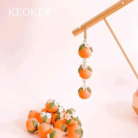 Handmade polymer clay orange bead earrings with floral accents hanging on display with a pile of matching beads below.