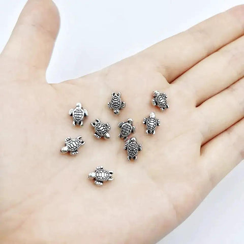 Hand holding 100 Pcs Dope Tiny Turtle Beads Antique Silver 0.9x0.7cm Mini Turtle Shaped Metal Beads For Crafts Jewelry Making Bracelets Necklaces Keychains DIY Supplies Great For Beading Projects And Gifts