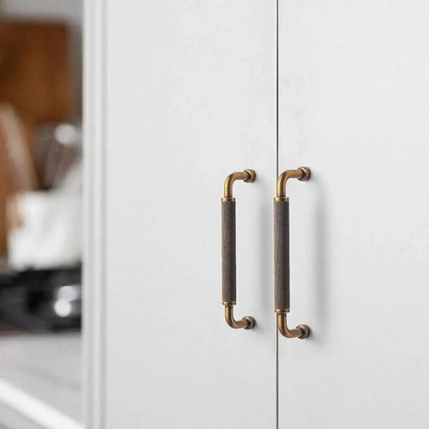 Installed 6 Pack 5 Inch Antique Brass Knurled Cabinet Pull Handles with textured non slip grip on white kitchen cabinet doors.