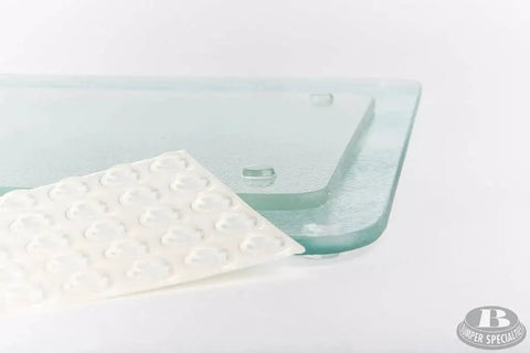 Sheet of clear self adhesive cylindrical bumper feet one half inch dia 0.14inch 50 pack next to glass object.