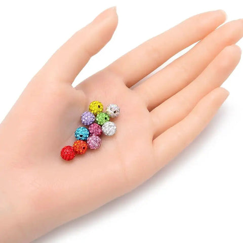 Hand holding colorful 8mm crystal rhinestone disco ball beads for jewelry making, ideal for 100 Pcs Suncatcher Crystal Rhinestone Disco Ball Beads 8mm Golden Shadow Polymer Clay Spacers For Shamballa Jewelry Making And All Craft Projects Perfect For DIY Jewelry Making Bead Embellishments Crafts And Party Decor.