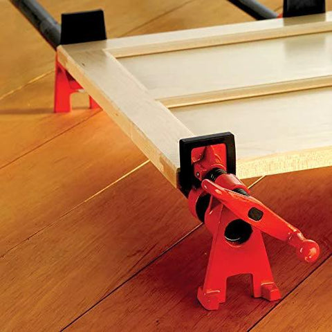 Red H-style pipe clamp, 3/4 in, securing wood panel in workshop setup
