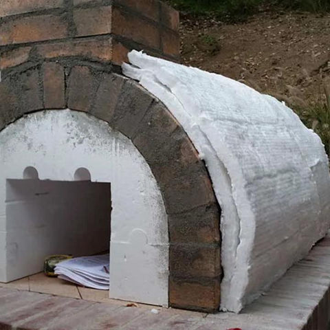 Ceramic fiber blanket insulation wrapped around a small brick oven/kiln, white exterior.