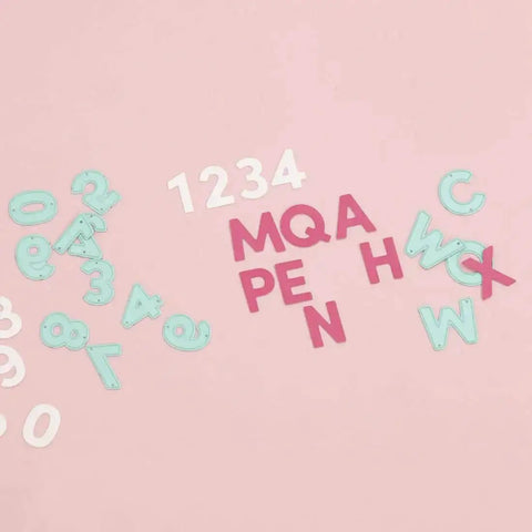 Die cuts of numbers and letters on pink surface, part of Number Shaped Die Cut Set, 0 Through 9, For Card Making And Scrapbooking