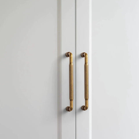 Antique Brass Cabinet Pull Handles Six Pack 5 Inch Vintage Vertical Grooved Textured Grip on white cupboard doors.