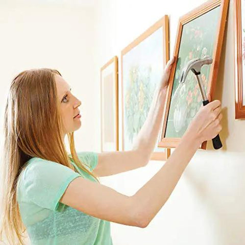 Woman using hammer to hang framed artwork on wall, showcasing DIY art projects with galvanized steel wire rope for crafts.