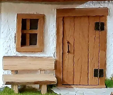 Miniature dollhouse with wooden door featuring brass hinges, matching window and bench, showcasing tiny craftsmanship details.