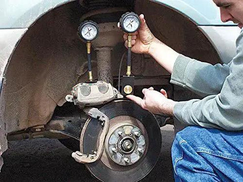 Front view of a black disc brake system analyzer in use on a car, with dual pressure gauges near the brake rotor.