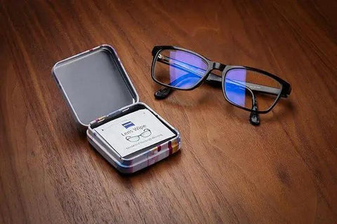 ZEISS Lens Cleaning Wipes Tin Boxes With Hinged Lids Pack Of Four next to eyeglasses on wooden surface