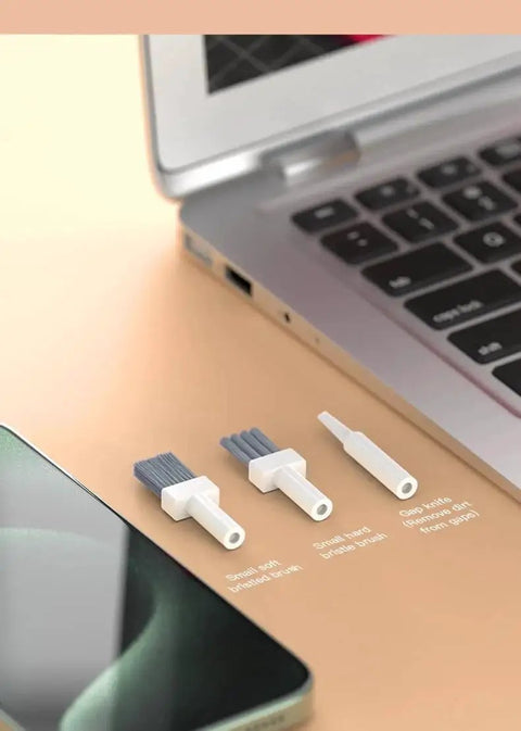 Three brush tools from 32-In-1 Compact Electronics Cleaning Kit for Keyboards, Phones, Monitors, Lenses next to a laptop and smartphone.
