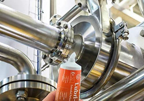 Haynes Lubri-Film Plus food-grade grease tube, orange 4 oz, shown with stainless steel industrial machinery