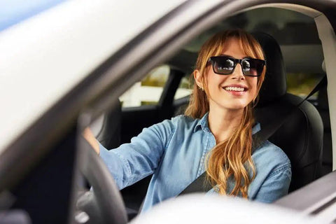 Woman driving car wearing sunglasses, representing ZEISS Pre-Moistened Sunglasses Cleaning Wipes For Smudge Removal 240 Count usage.