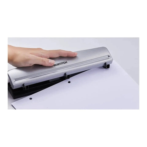 Hand using Rock Solid 3 Hole Punch for office and home use with 12 sheet capacity, heavy duty metal construction, rubber base, sleek silver finish.