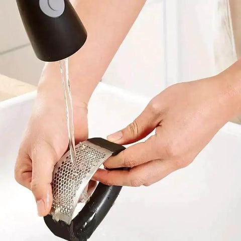 Person washing stainless steel garlic press rocker mincer with peeler under faucet, showcasing easy cleanup and rust resistance