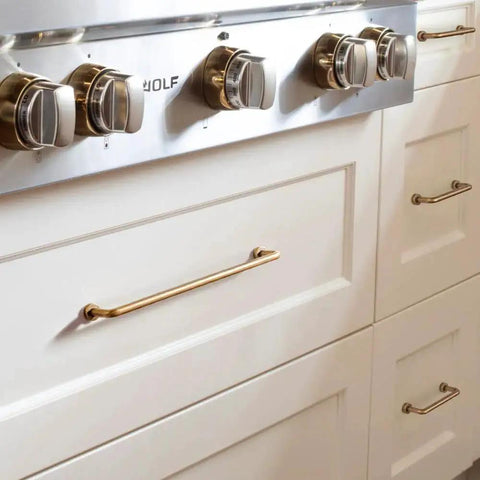 Set Of 12 SleekTouch Antique Brass Cabinet Pulls, 3 3/4 Inch Center To Center installed on white kitchen drawers near stove